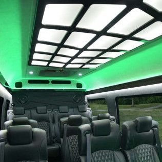 Interior of a luxury van with black leather seats, green neon lights, and a grid-pattern ceiling.