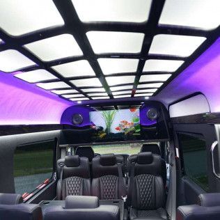 Interior of a luxury van with black leather seats, an aquarium, and purple overhead lighting.