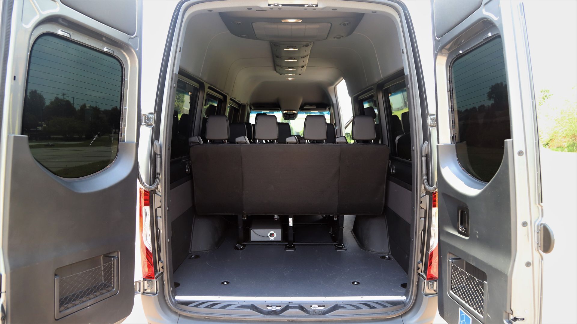 Interior view of a gray van with open doors; rear seats, windows, and empty cargo area are visible.