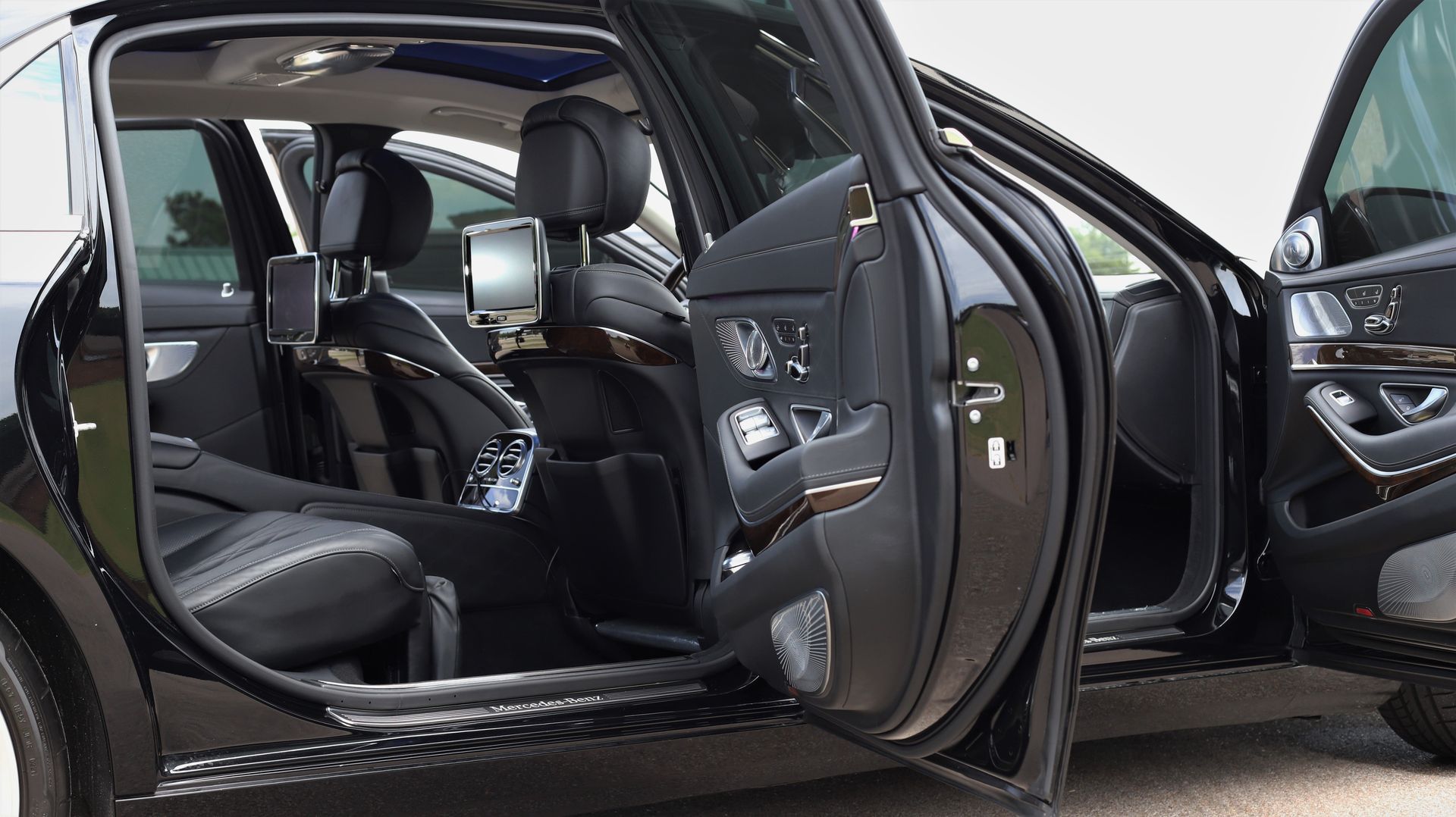 Black luxury car interior with open doors, leather seats, and mounted screens.
