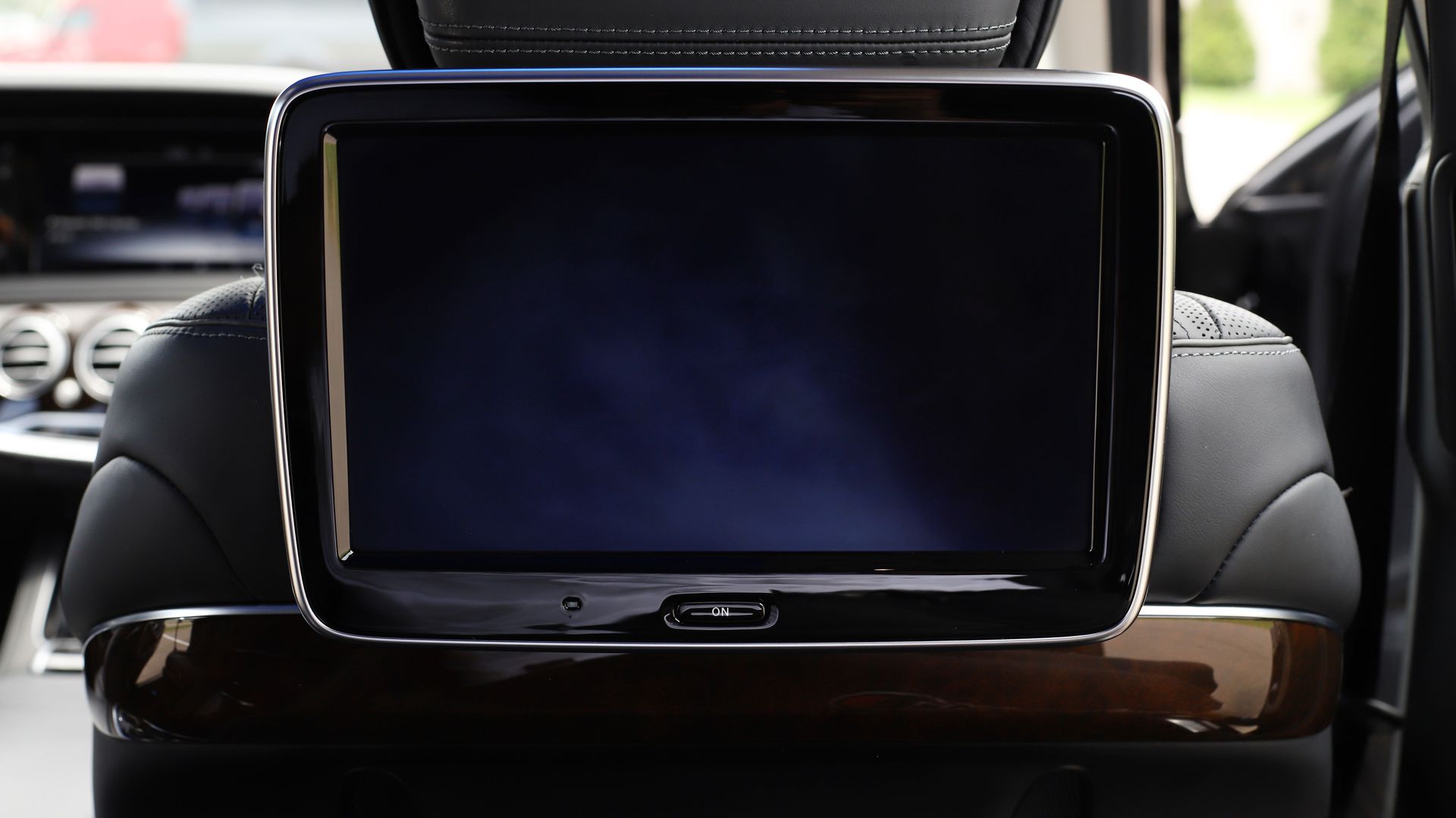Car's back seat featuring an entertainment screen mounted on the headrest. Black and brown interior with a blurry background.