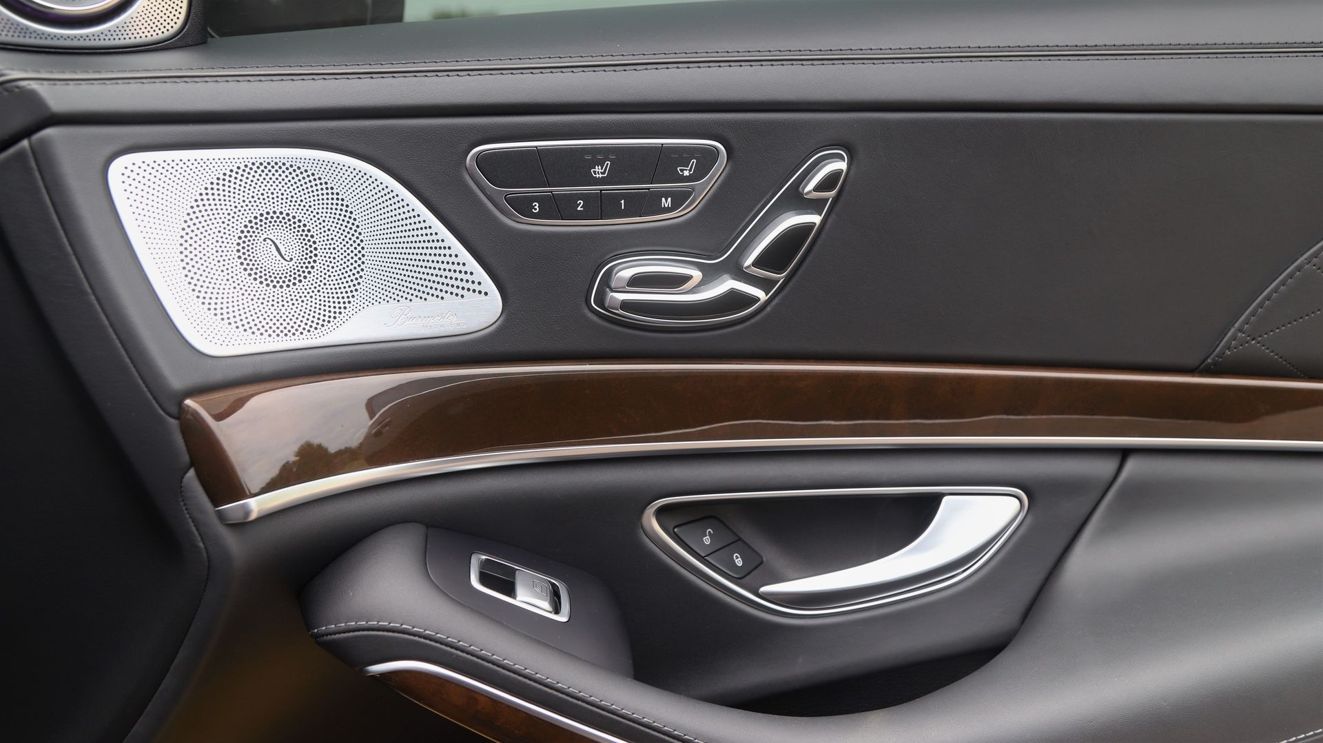 Car door interior with wood trim, seat controls, speaker grill, and door handle.