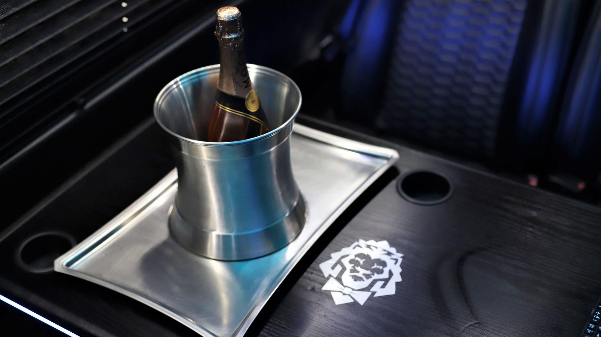 Champagne bottle in a metal ice bucket on a serving tray inside a luxury vehicle.