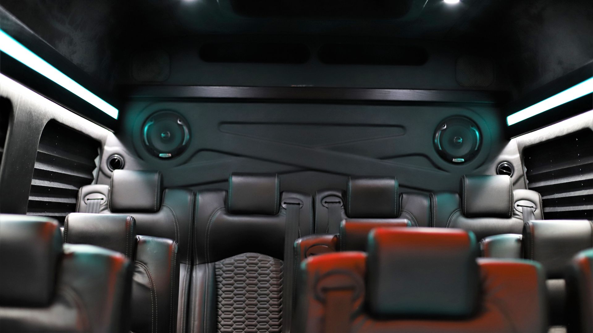 Interior of a black van with rows of leather seats. Blue and red lighting.