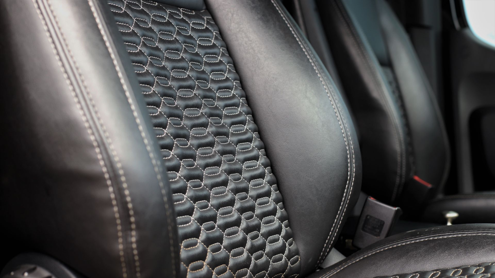 Black leather car seat with white stitching and patterned center.