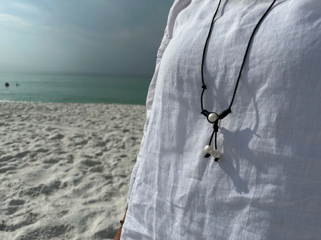 A person wearing a white shirt and a black necklace is standing on a beach.