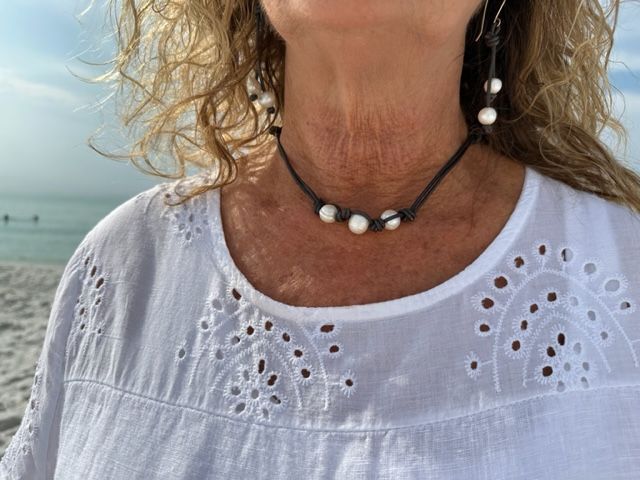 A woman wearing a choker and earrings is standing on the beach