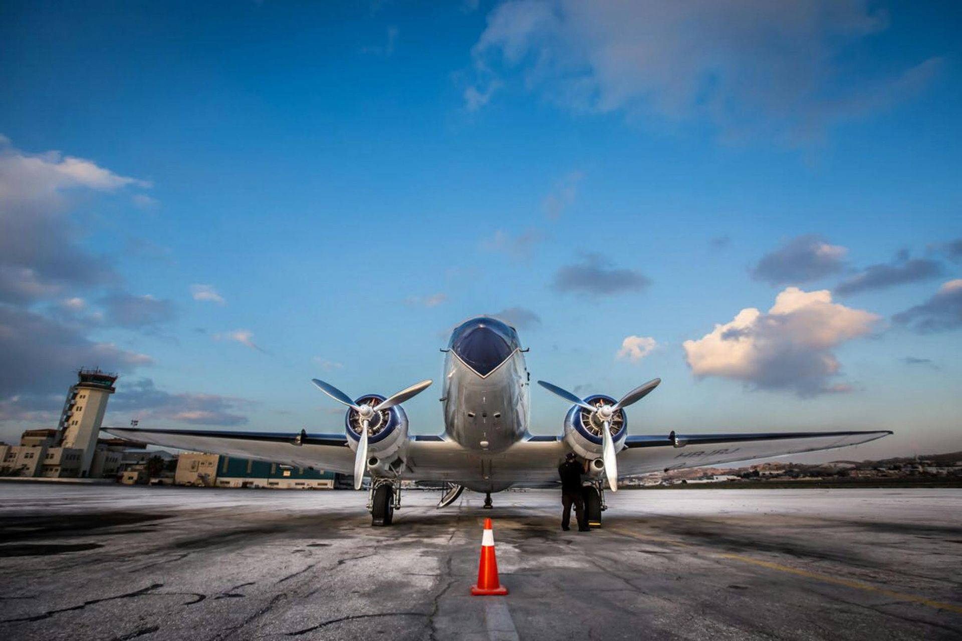 Front view of a twin-engine airplane on the tarmac under a blue sky, with an orange cone in front.