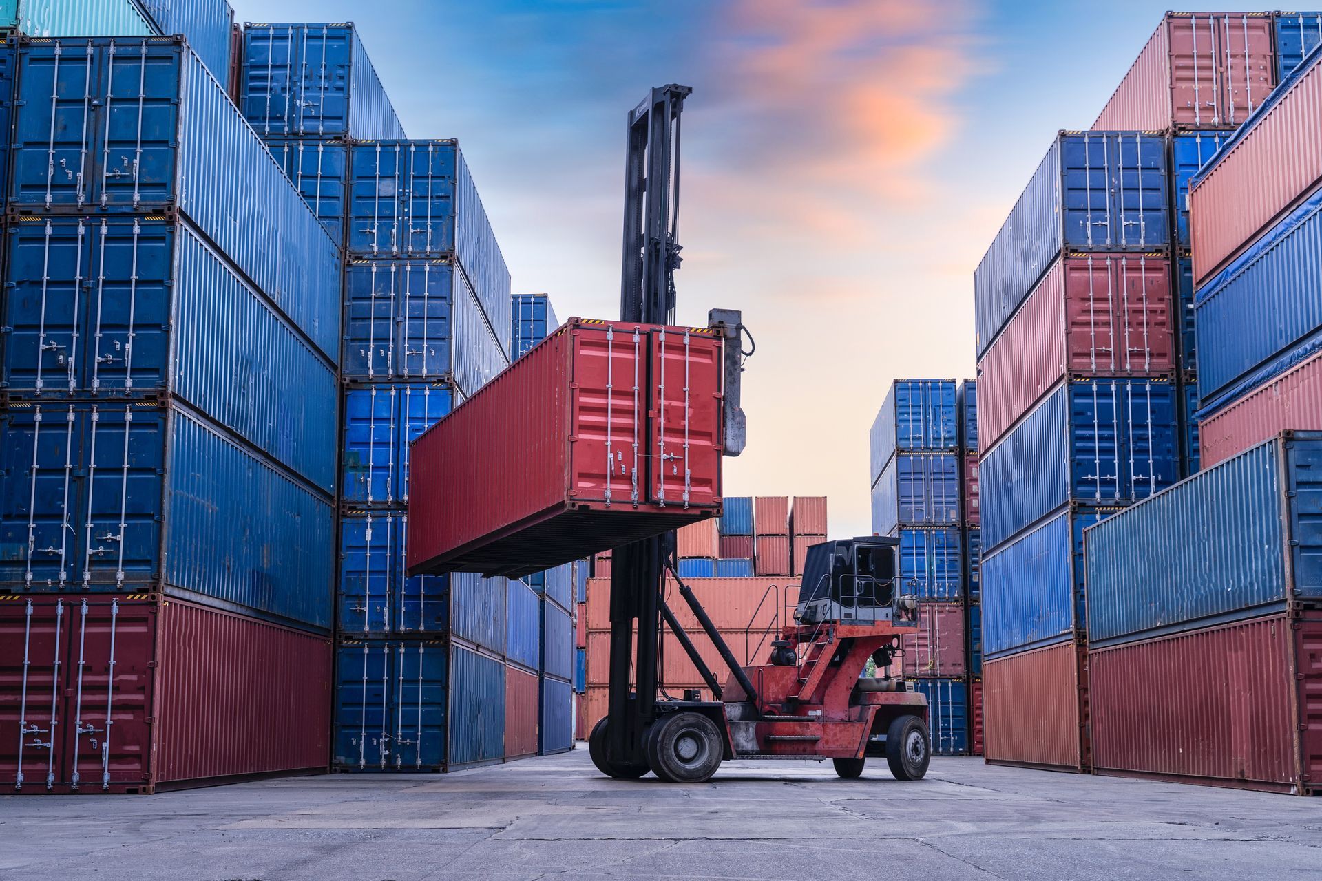 A forklift is lifting a container in a warehouse filled with lots of shipping containers.