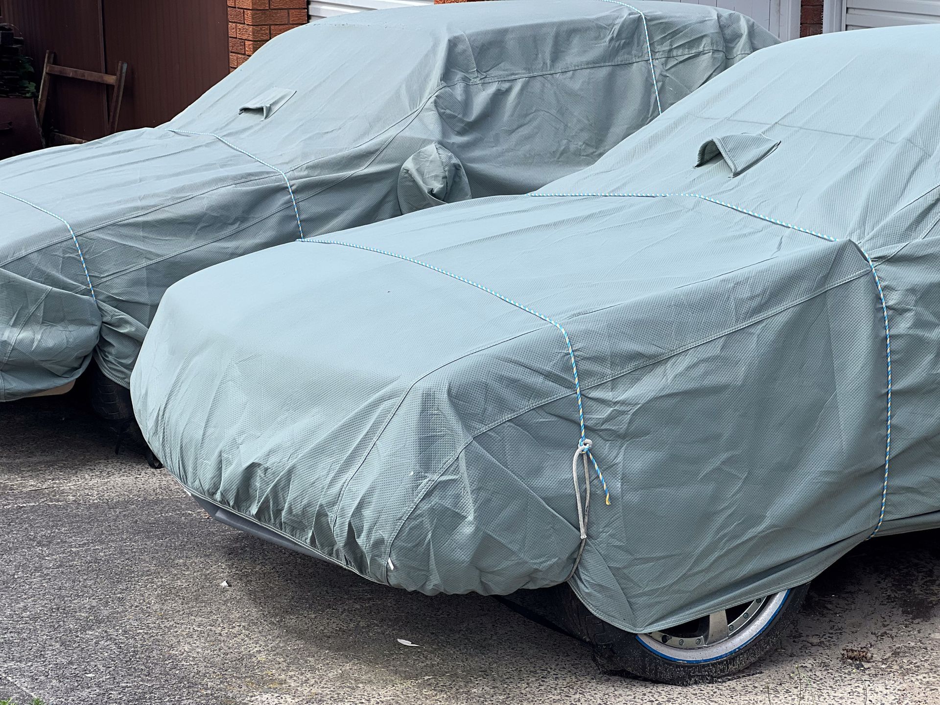 Two cars are parked next to each other with covers on them.