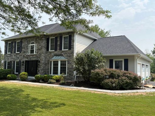 Two-story house with stone facade, black shutters, and a green lawn under a sunny sky.