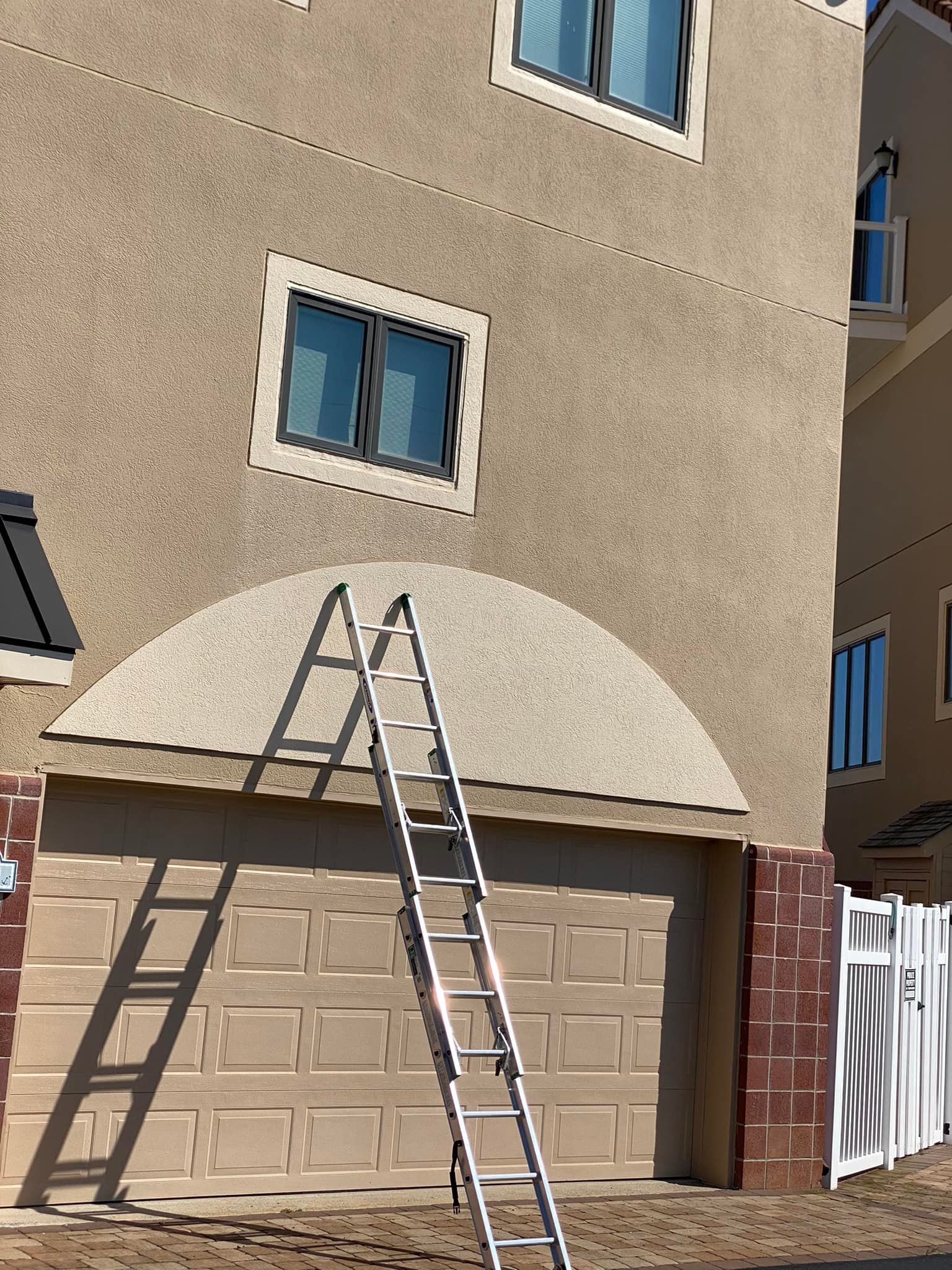 Ladder leaning against beige stucco wall above a garage door.