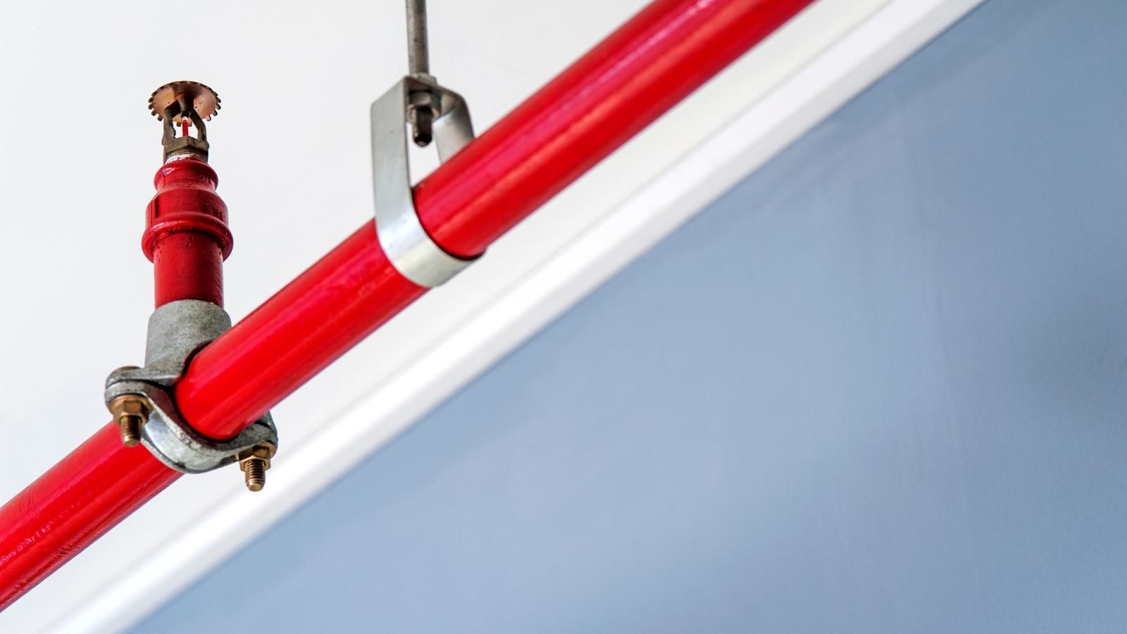 A red pipe with a fire sprinkler attached to it is hanging from the ceiling.