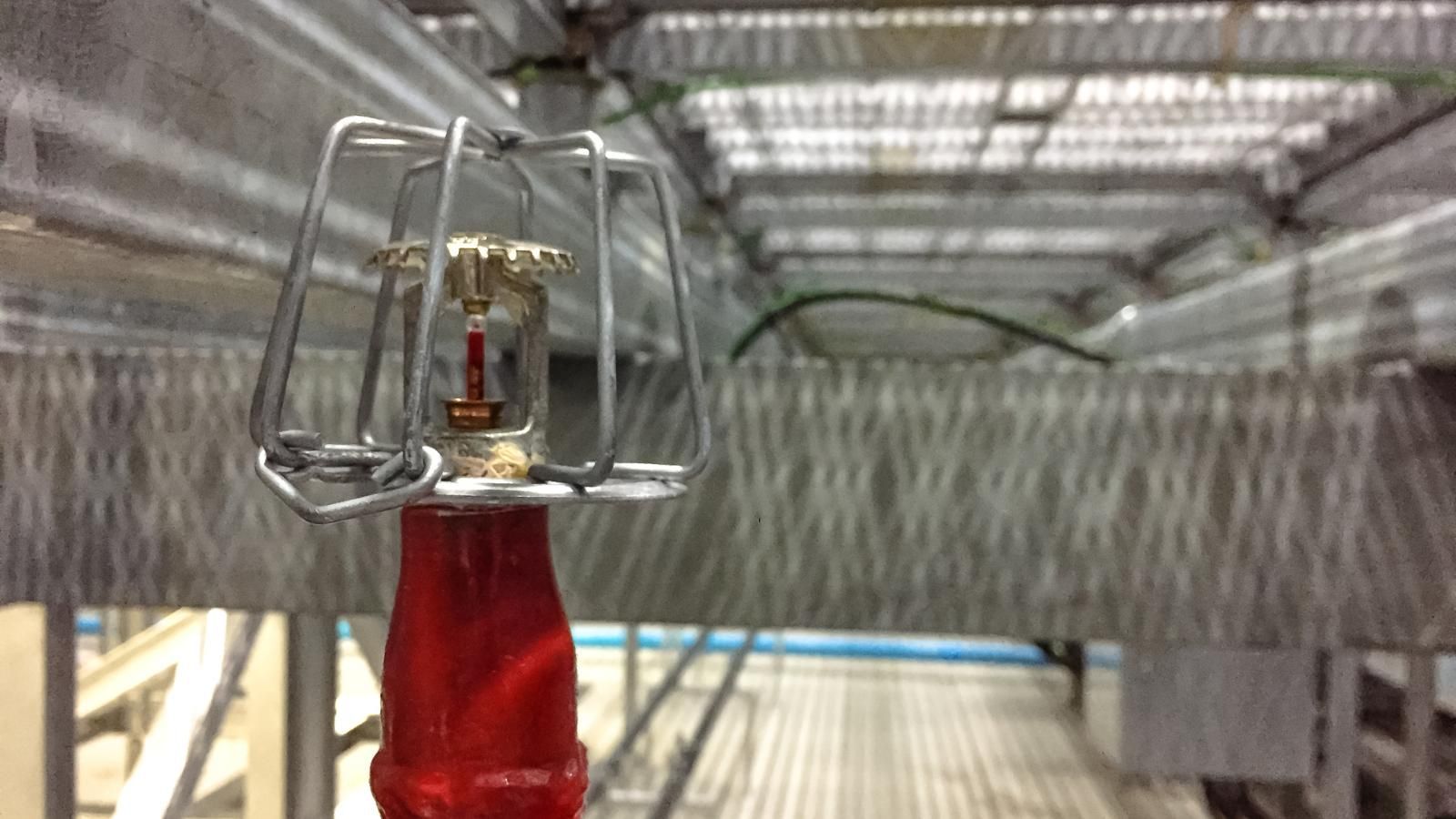 Close-up of a mechanical device with red base in front of a blurred metal walkway or grid structure