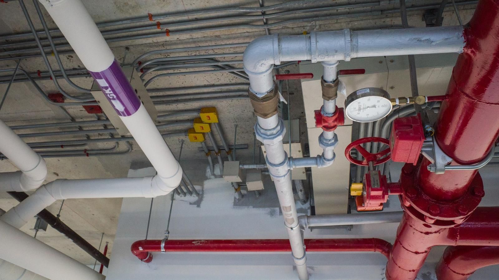 how to test fire sprinklers Overhead view of pipes and wires in an industrial setting; red, white, gray, and purple.