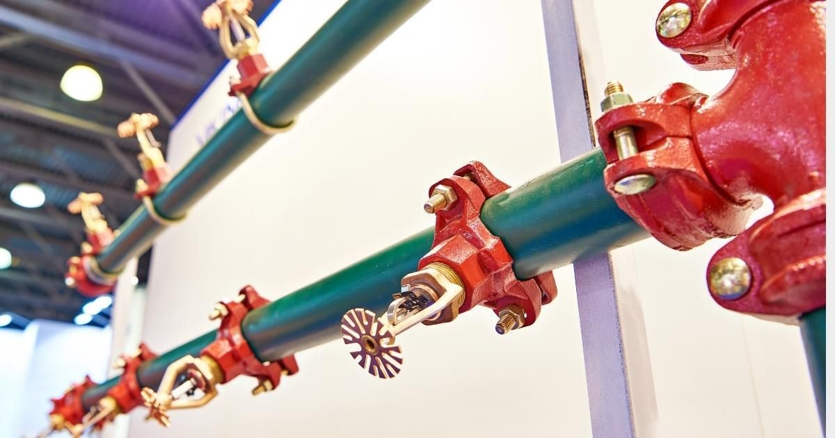 Green pipes with red sprinkler heads, mounted on a white wall, likely a fire safety system.