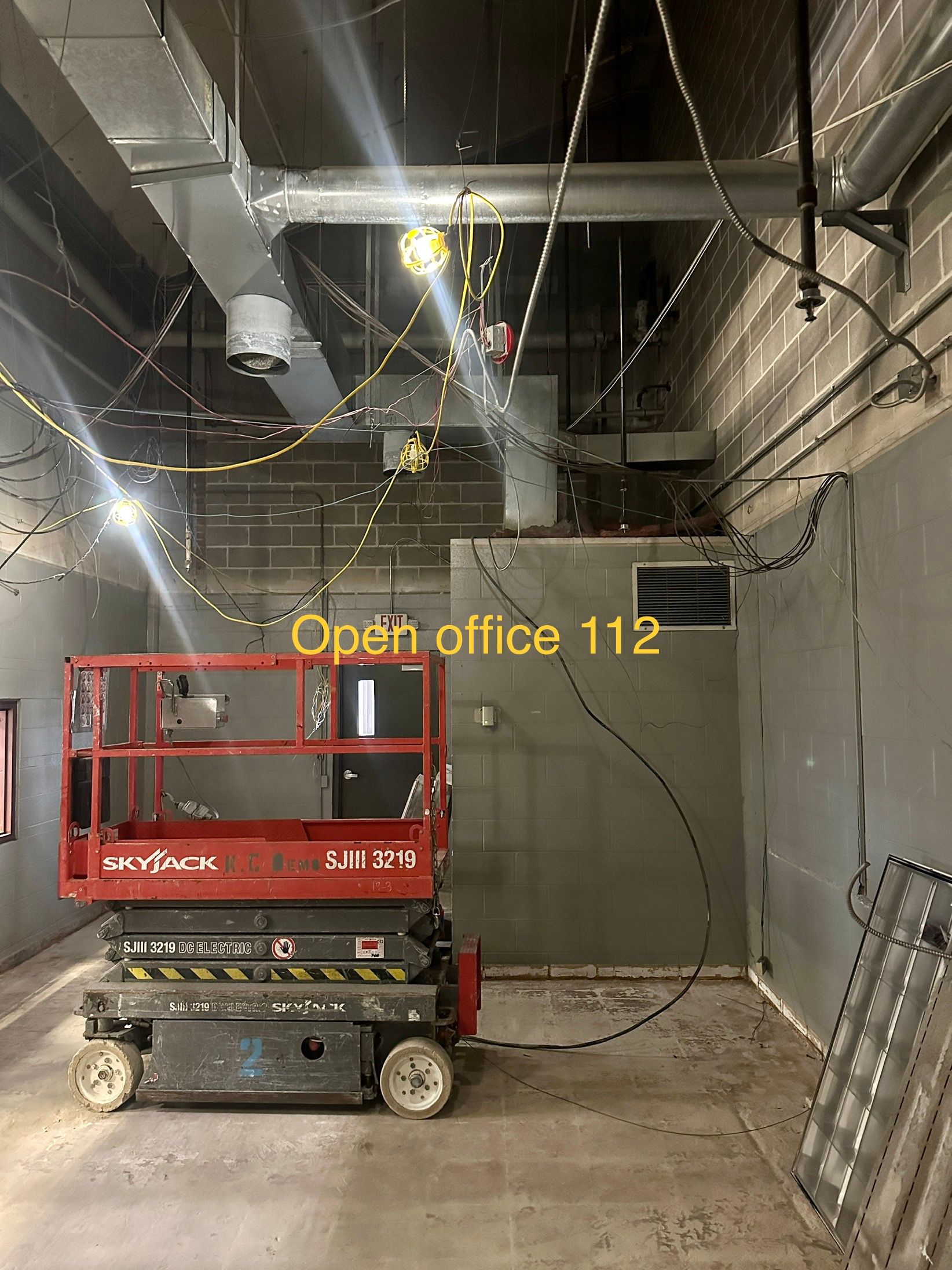 A scissor lift is sitting in a room with a sign that says open office 112.