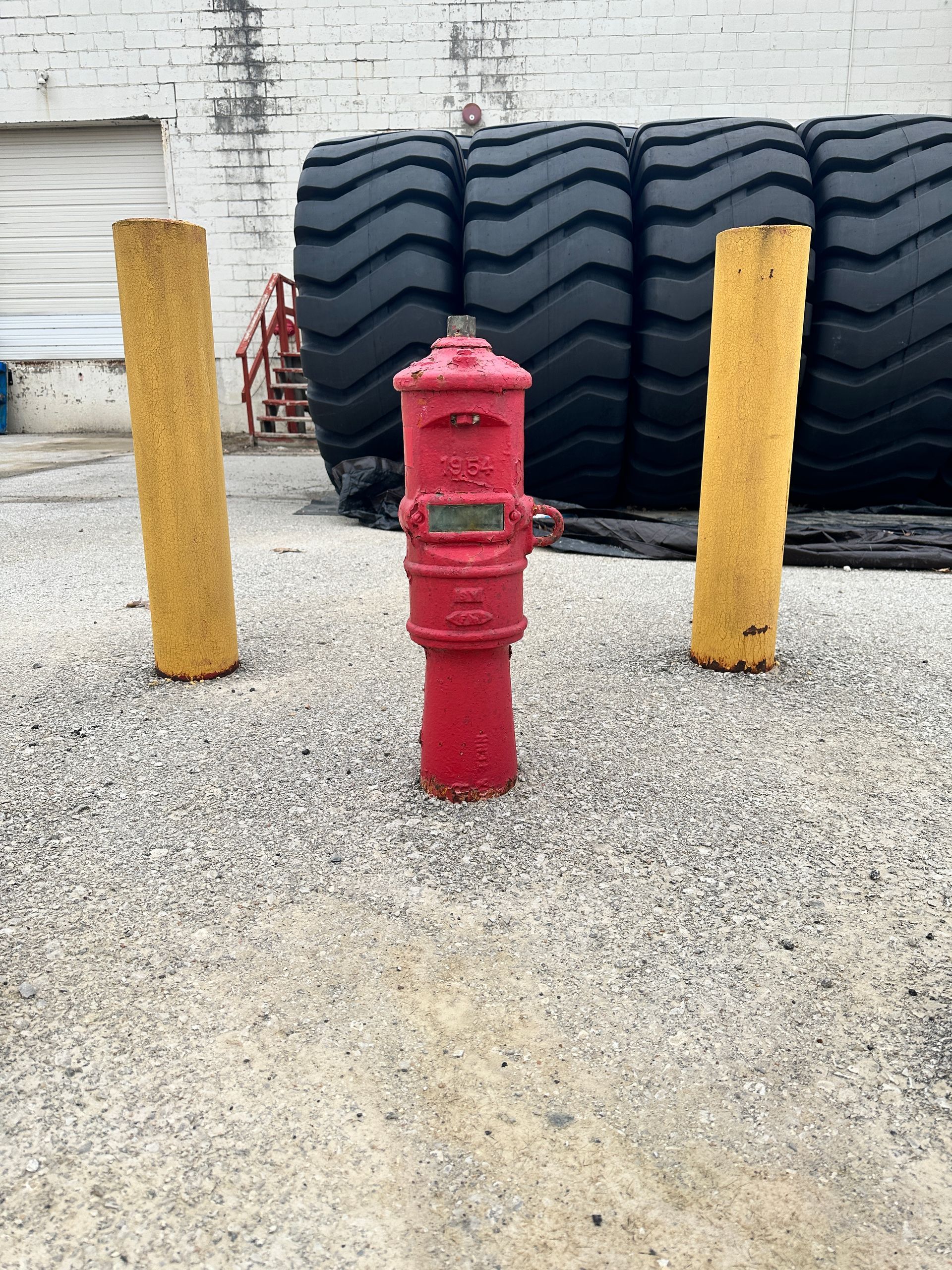A red fire hydrant is in a gravel area in front of a pile of tires.