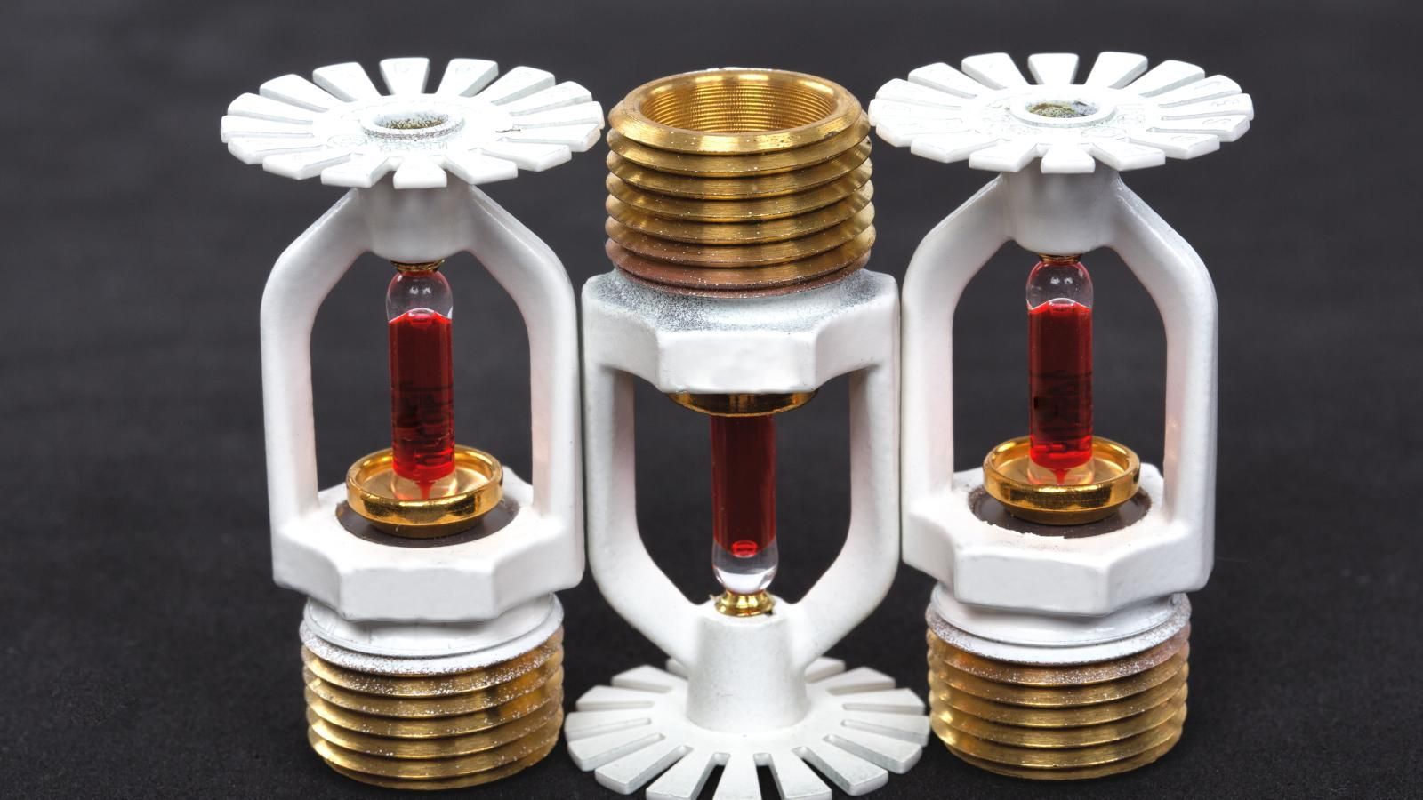 Three fire sprinklers are sitting next to each other on a black surface with two being heads up.