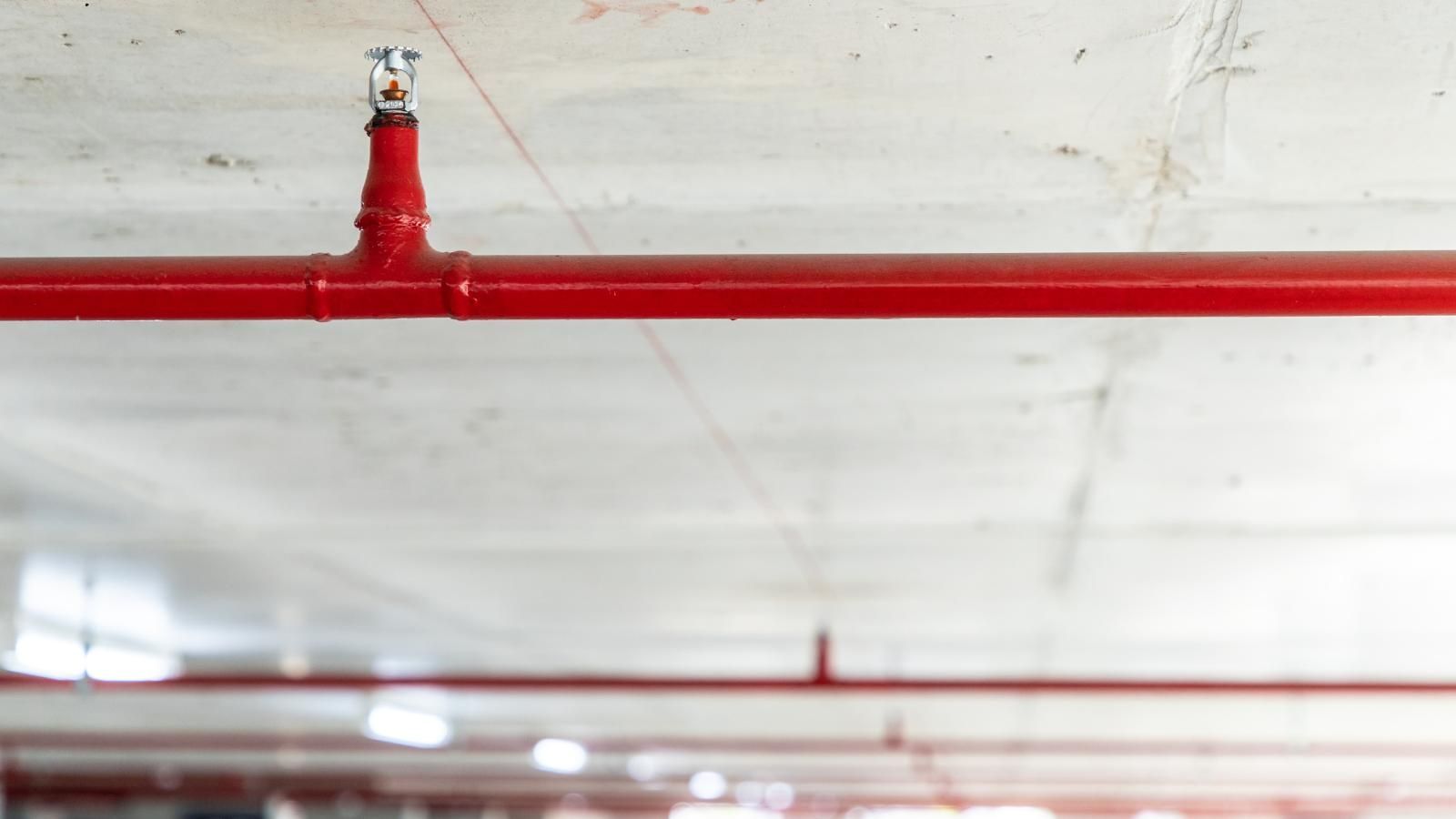 A red fire sprinkler is hanging from the ceiling of a building.