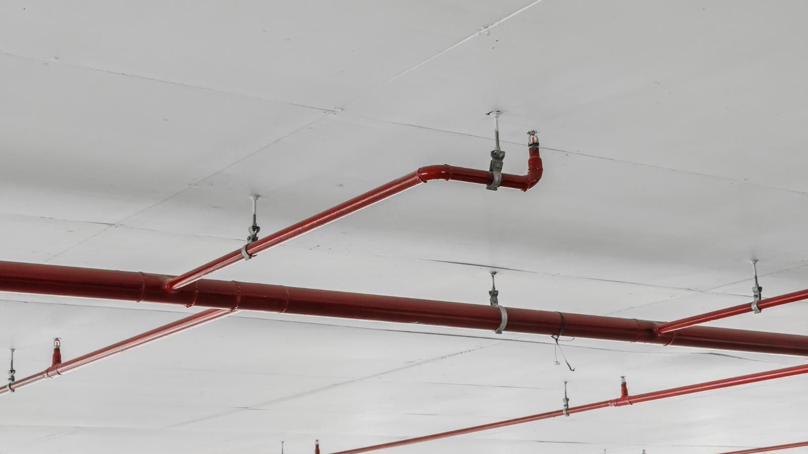 Red fire sprinkler pipes and ceiling fixtures running across a white ceiling in an indoor space
