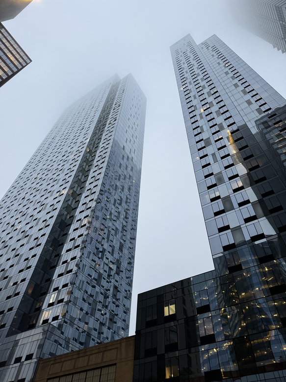 Skyscrapers against a bright blue sky with scattered clouds, reflecting the sky in their glass exteriors.