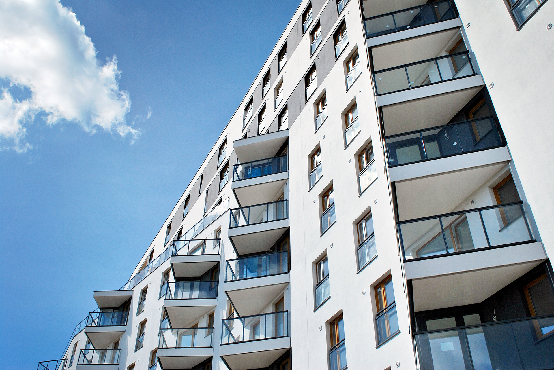 White high-rise apartment building with multiple balconies against a blue sky with fluffy clouds.
