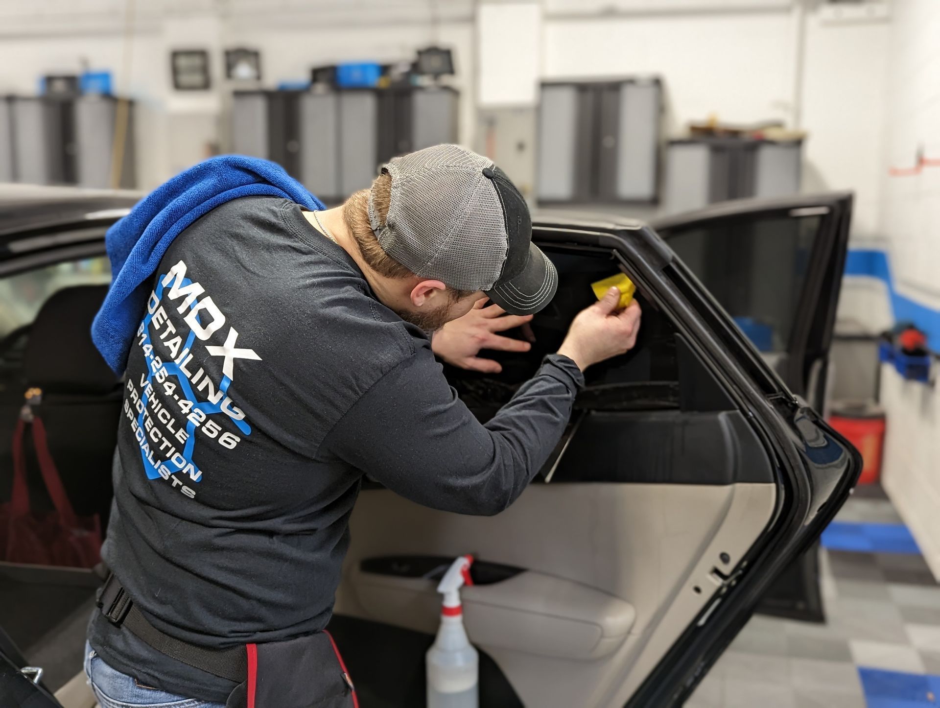 a man is applying window tinting to a car door .a blue bmw m2 is driving on a snowy road .  Ceramic coating, PPF, Tint, Vinyl Wrap, johnstown pa www.mdxdetailing.com