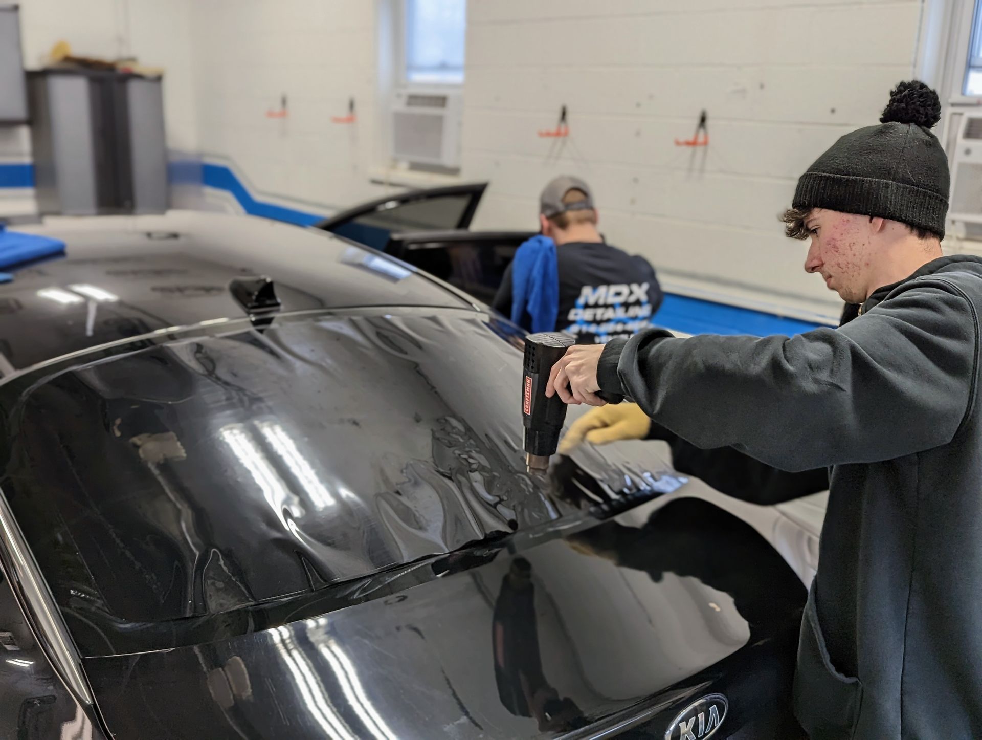 a man is cleaning the windshield of a black car . Ceramic coating, PPF, Tint, Vinyl Wrap, johnstown www.mdxdetailing.com