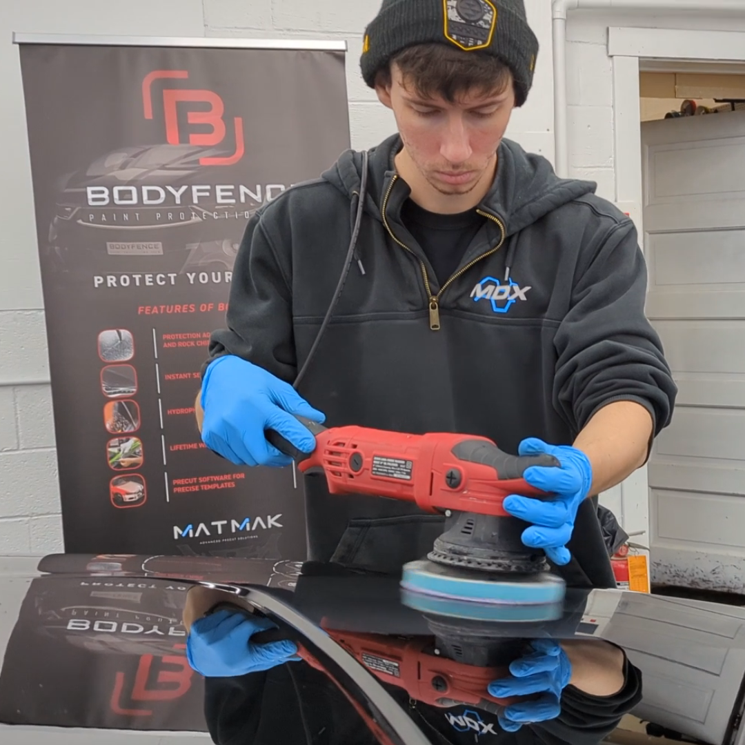 a man is polishing a car in front of a bodyfence sign. Ceramic coating ppf johnstown pa