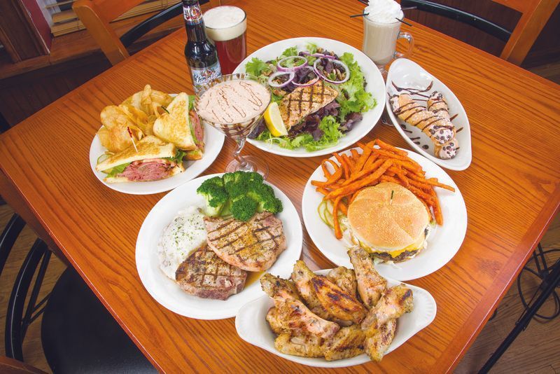 Table set with various dishes: sandwich, salad, burger, wings, steak, sweet potato fries, and desserts.
