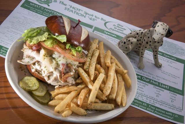 Sandwich and fries on a plate with pickles, next to a spotted dog figurine and menu.