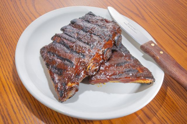 Barbecued ribs on a white plate with a knife on a wooden table.
