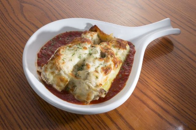Stuffed shells baked in marinara sauce, topped with melted cheese, served in a white dish on wood.