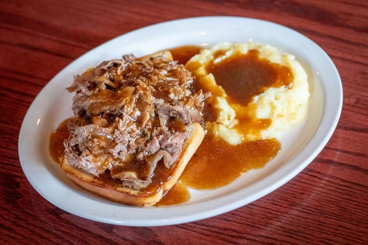 Roast beef sandwich with gravy, beside mashed potatoes, on a white plate.