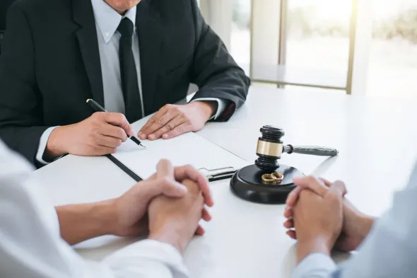 A lawyer signing paperwork with clients, gavel present on a table.