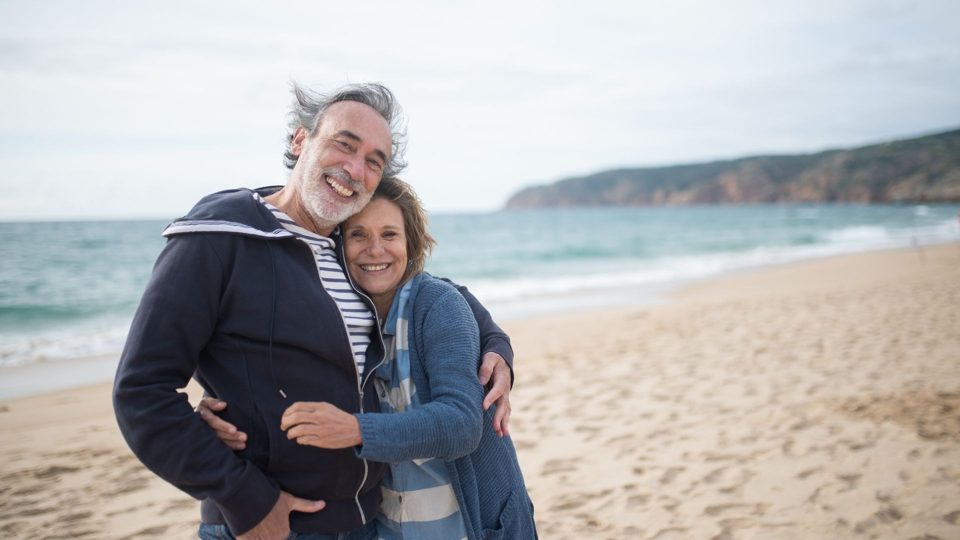A man and a woman are posing for a picture on the beach.