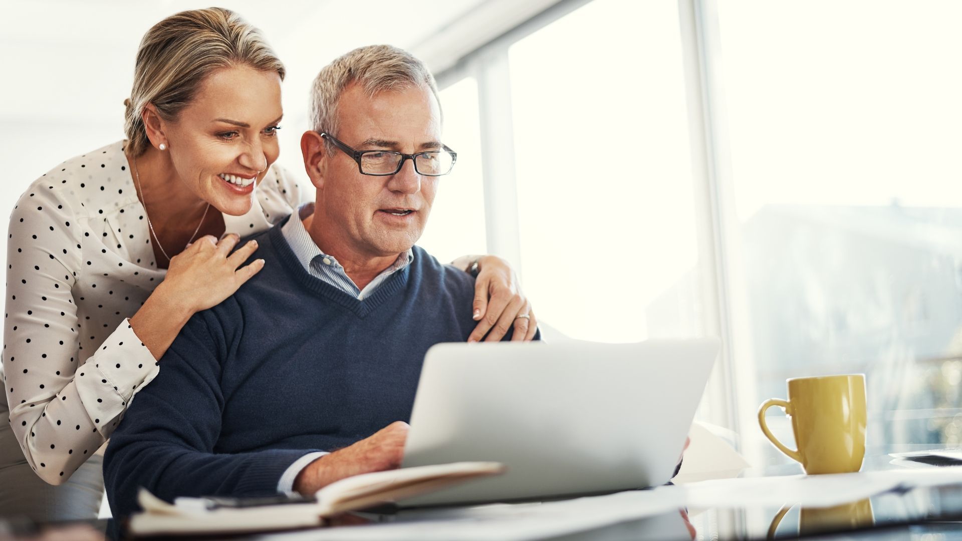A woman is standing next to a man using a laptop computer.