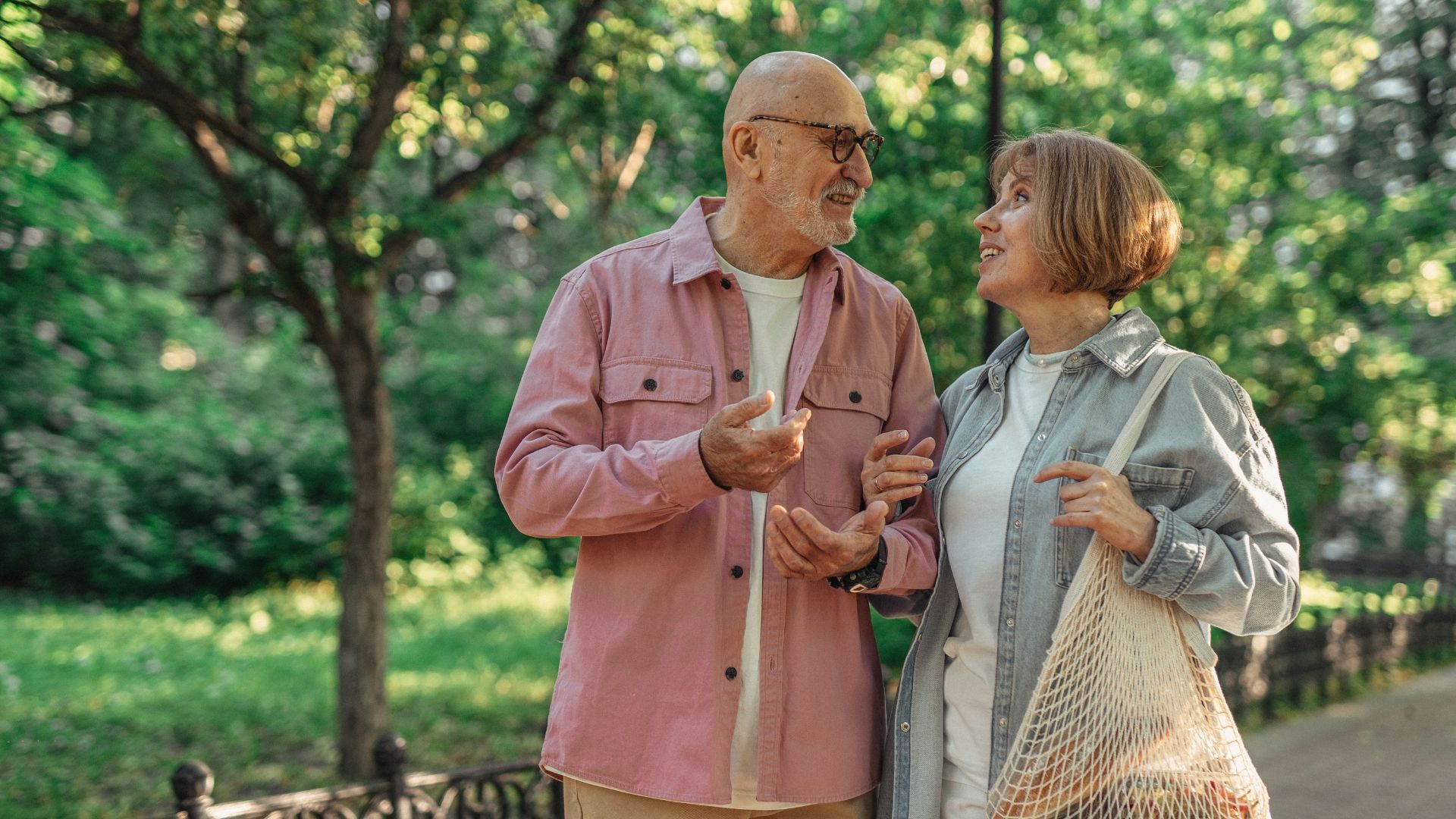 An elderly couple is walking in a park and talking to each other.