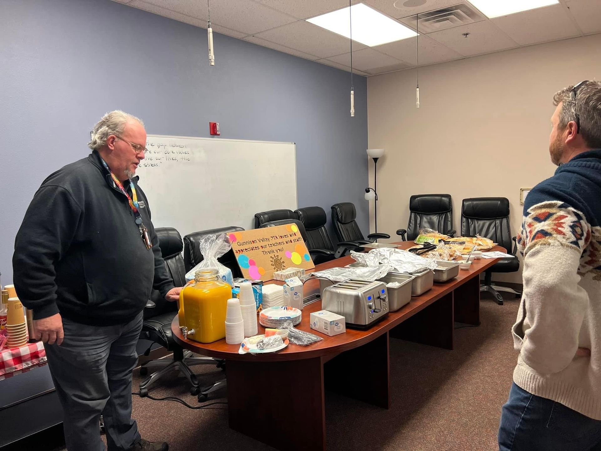 Two men are standing in front of a long table in a conference room.