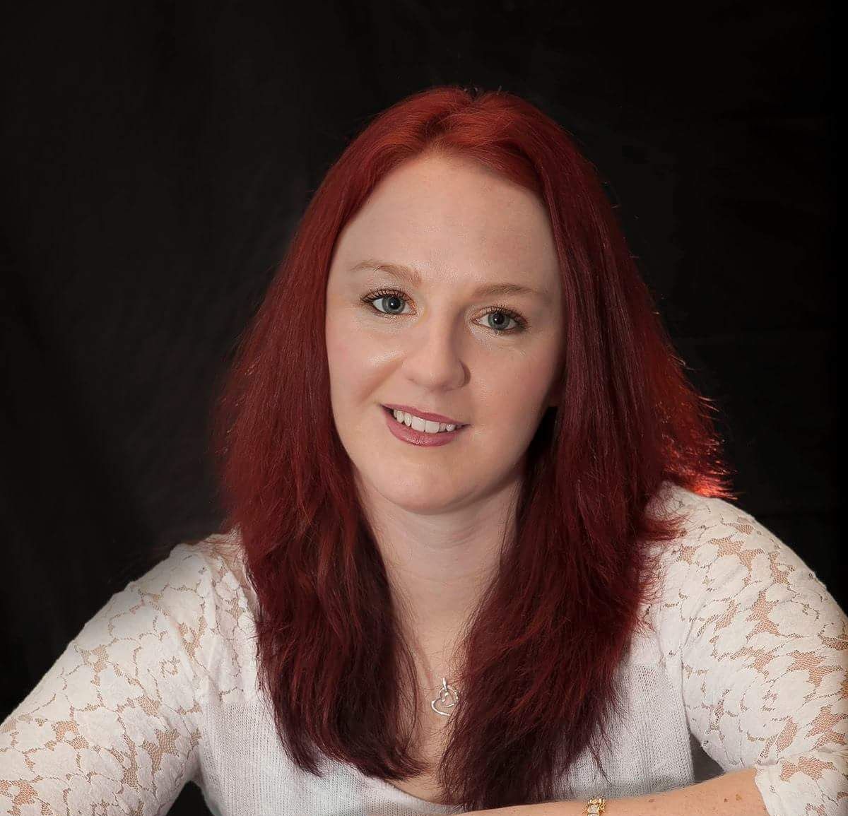 A woman with red hair is wearing a white lace top