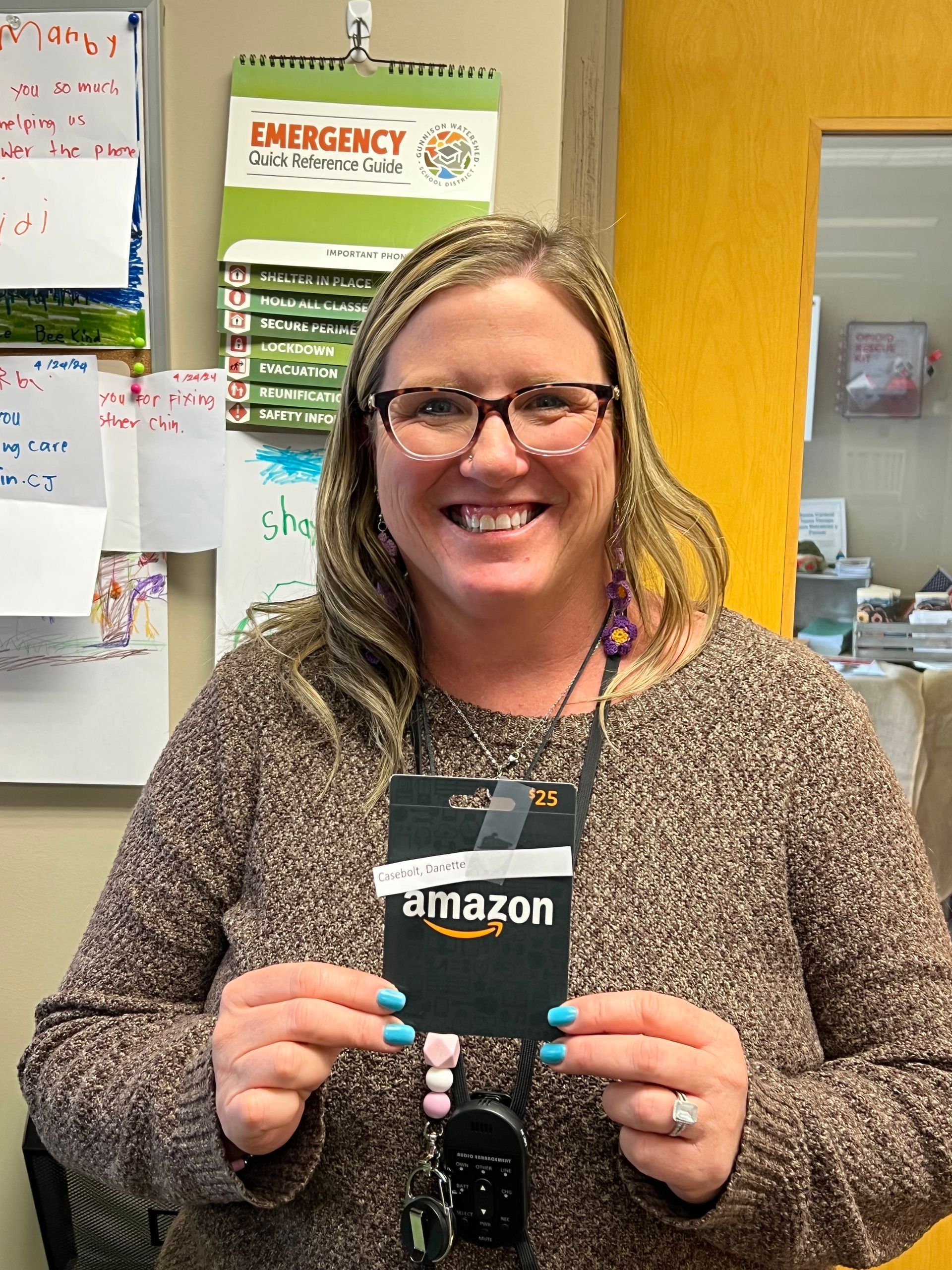 A woman in a brown sweater is holding an amazon gift card