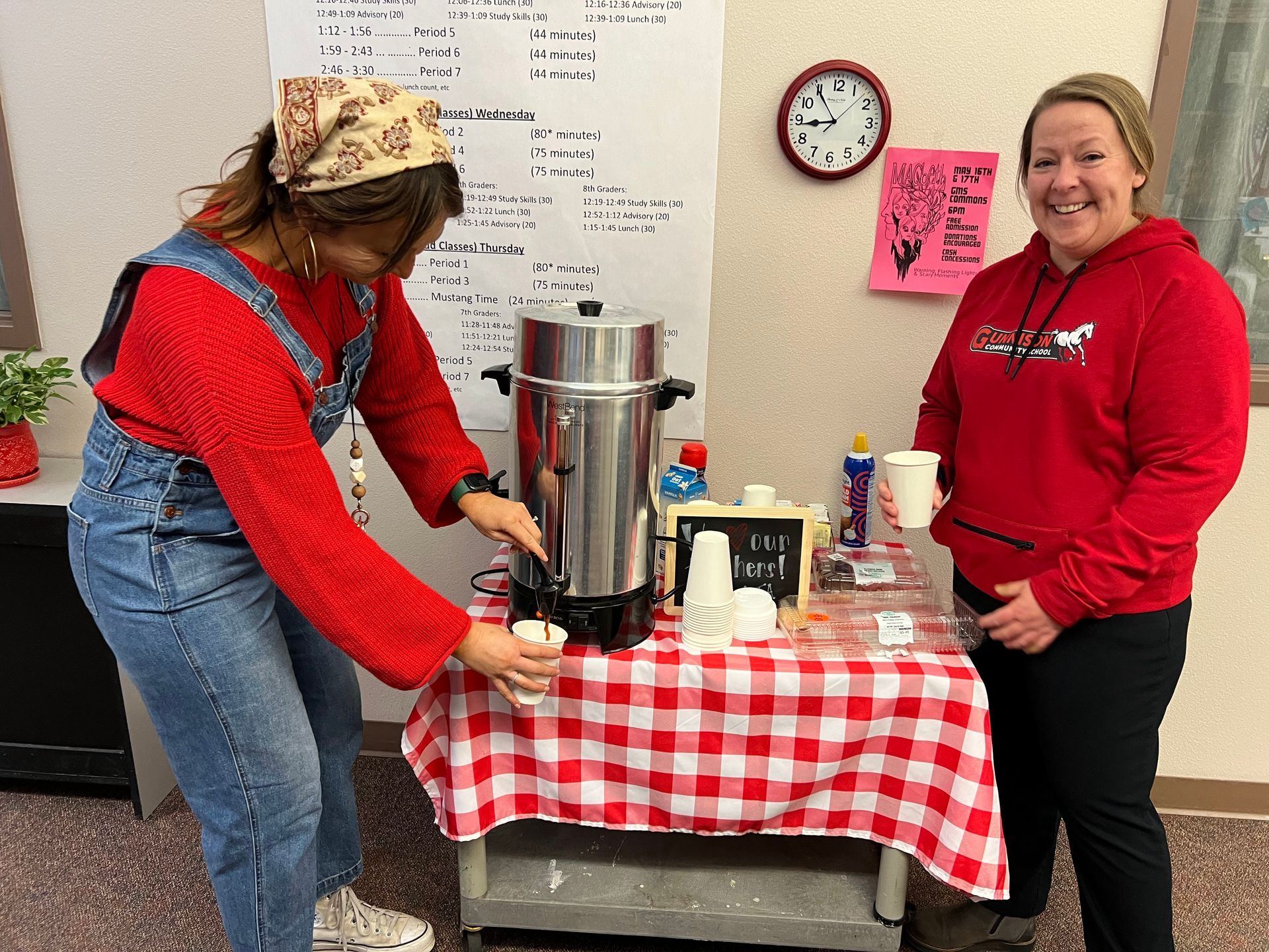 Two women are standing next to a table with a coffee pot on it.