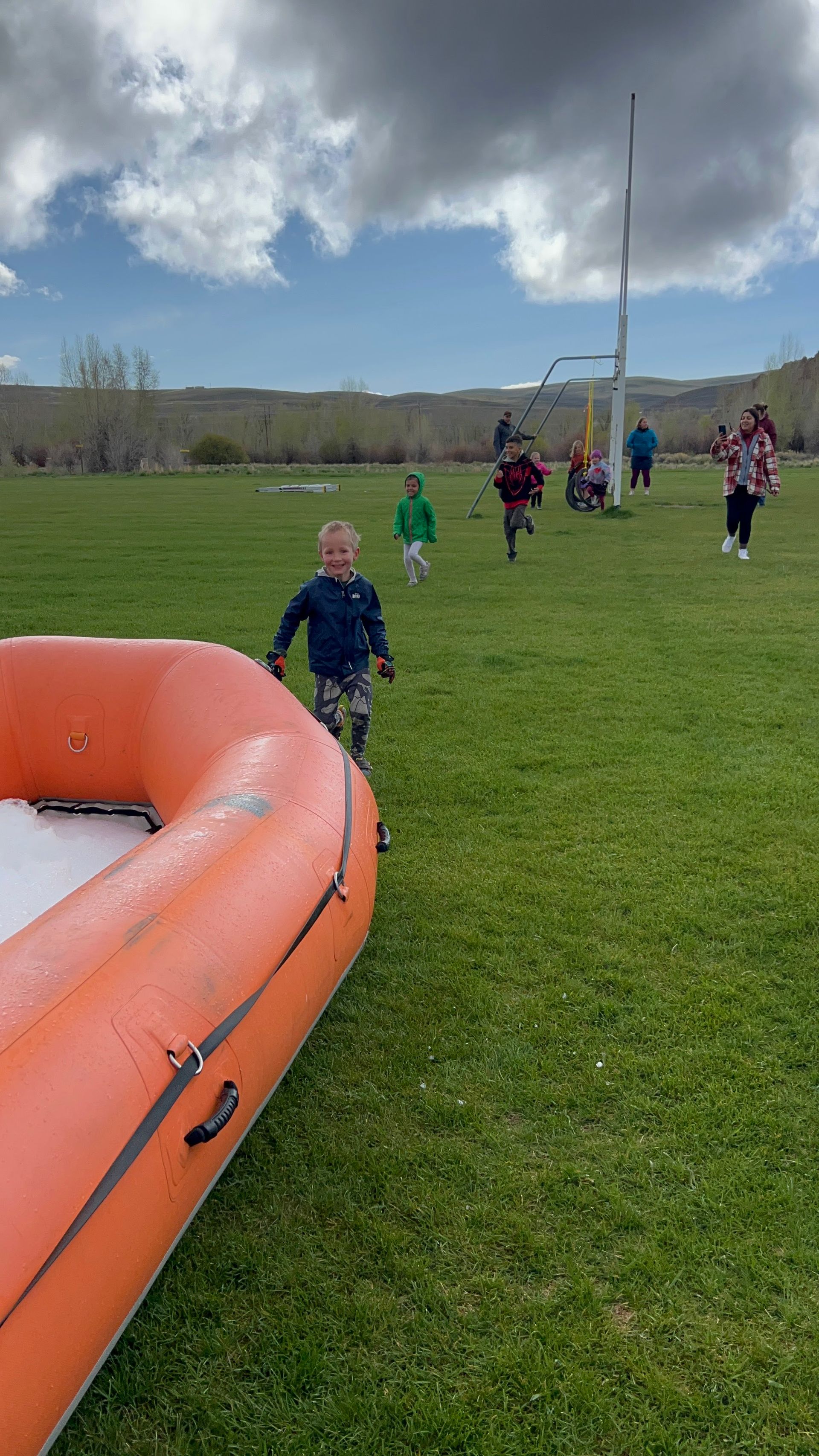 A group of children are running in a field next to an inflatable boat.