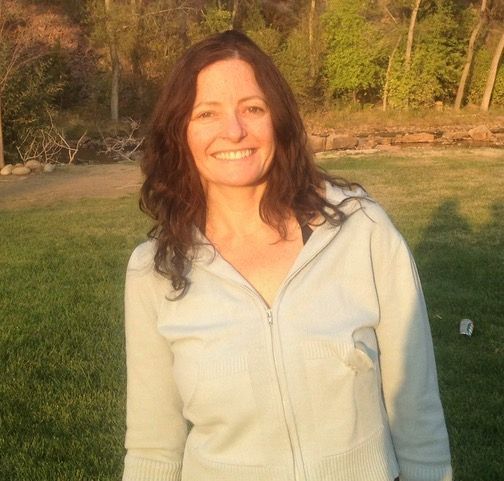 A woman in a white sweater is smiling in a field