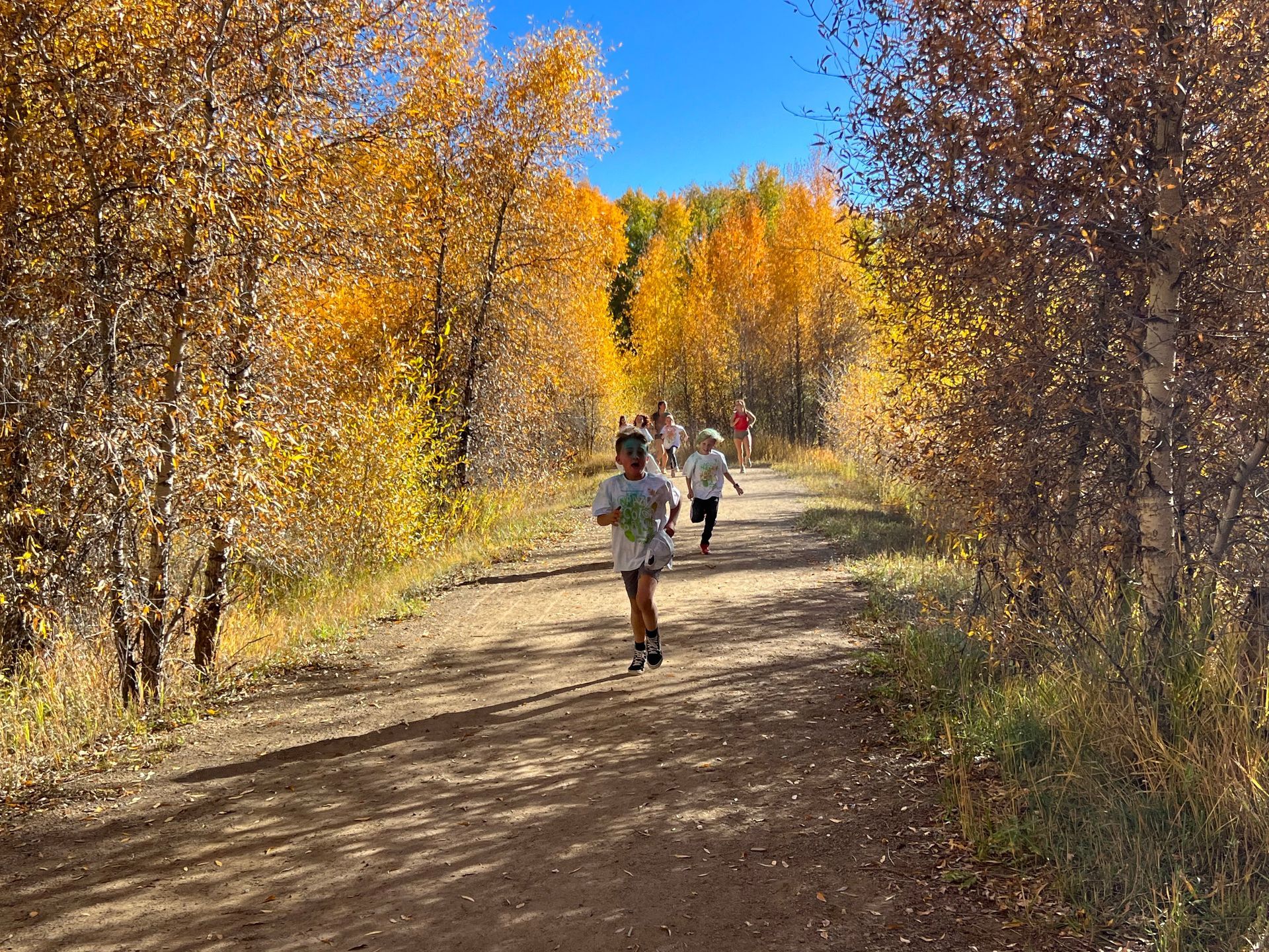 A group of people are running down a dirt road in the woods.