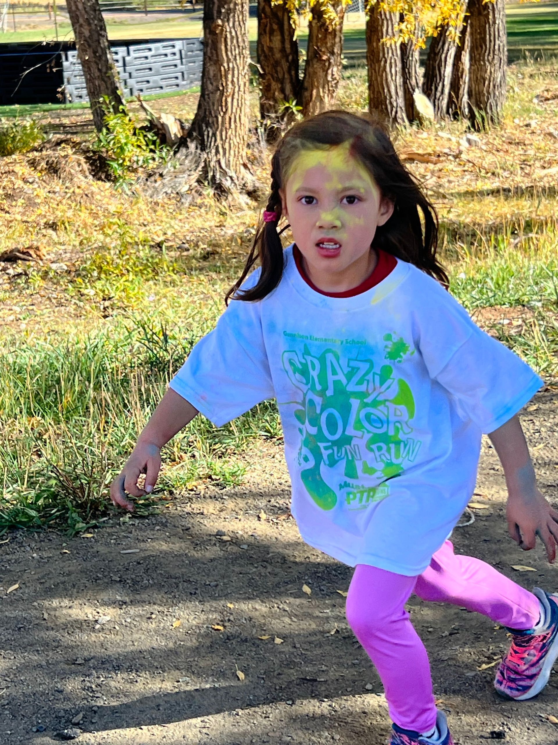 A little girl with powder paint on her face is running in a park.