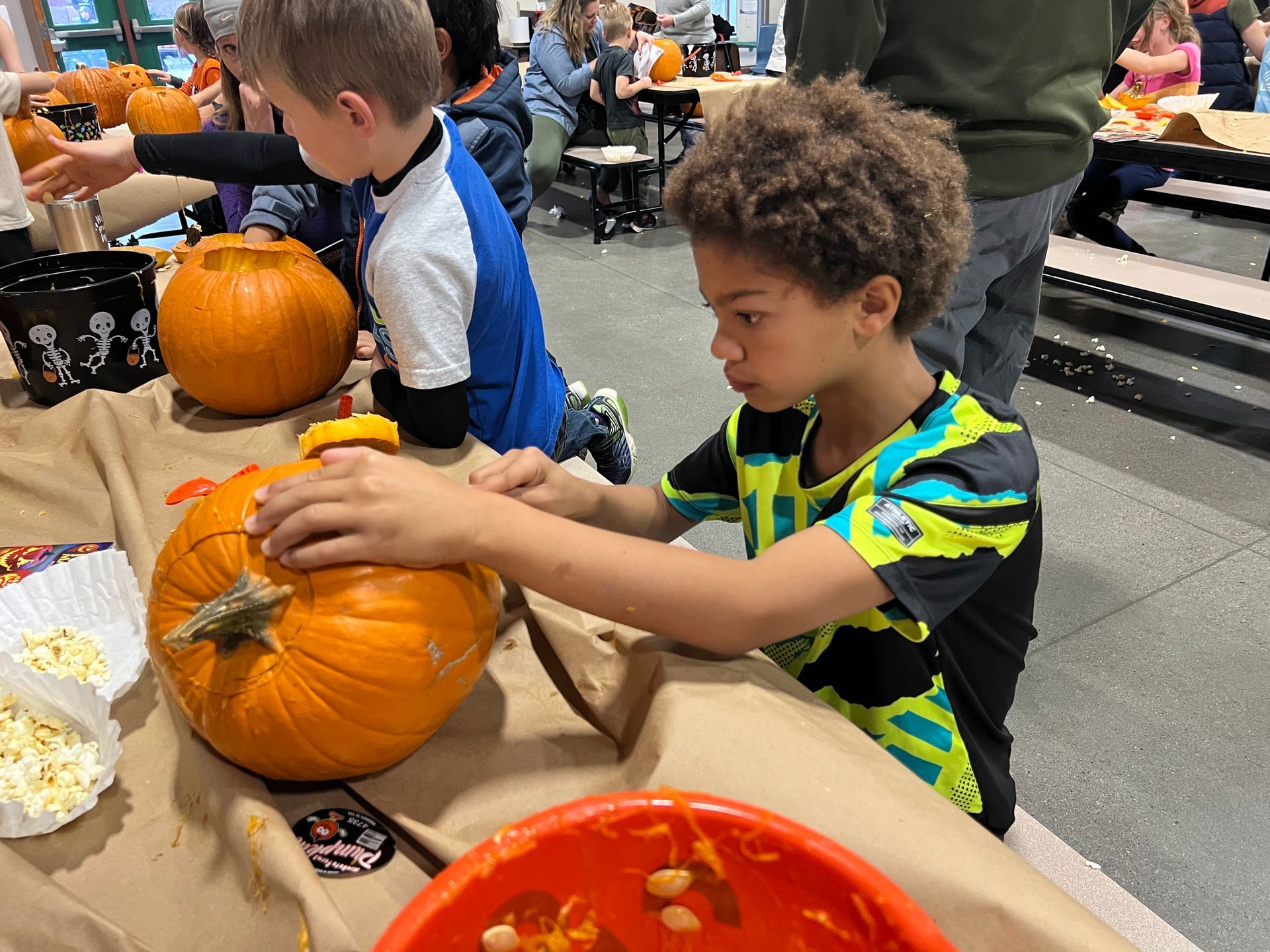 A young boy is carving a pumpkin at a table.