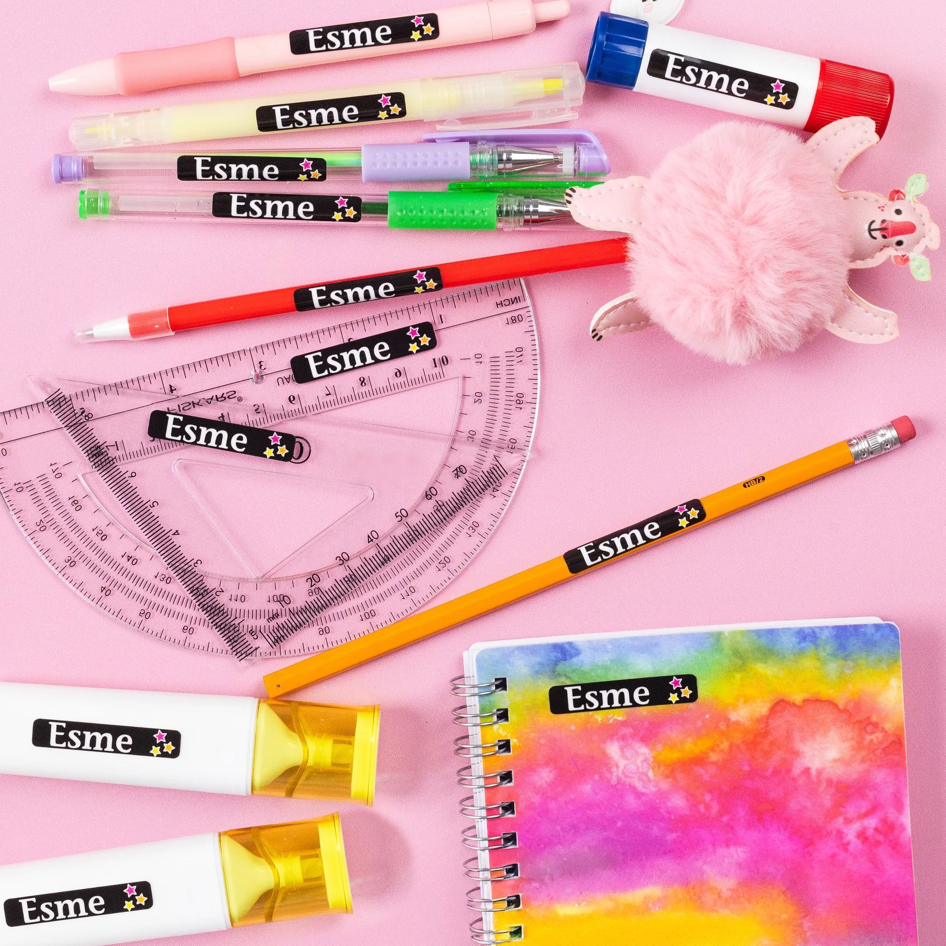 School supplies with name labels. Pens, highlighters, protractor, and notebook on pink surface.