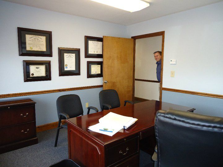A man is standing in a room with a desk and chairs
